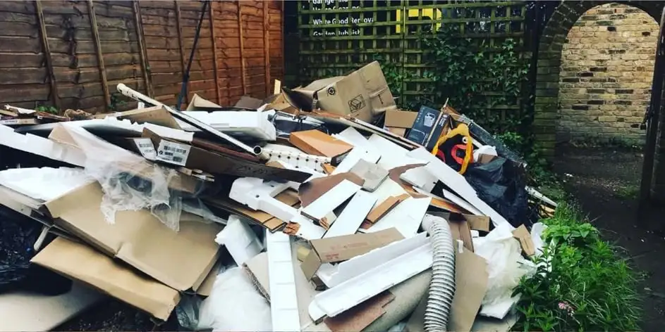 Before: A heap of white plastic trim, cardboard, timber and pipe filling a back garden by a brick archway and trellis
