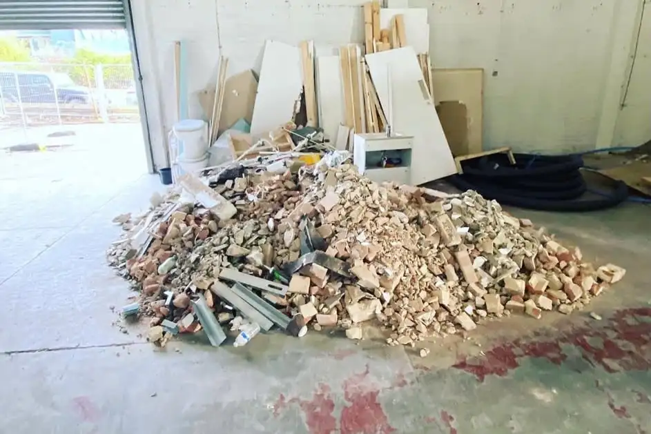 A pile of broken bricks and rubble with timber, boards and metal studs on the floor of an industrial unit