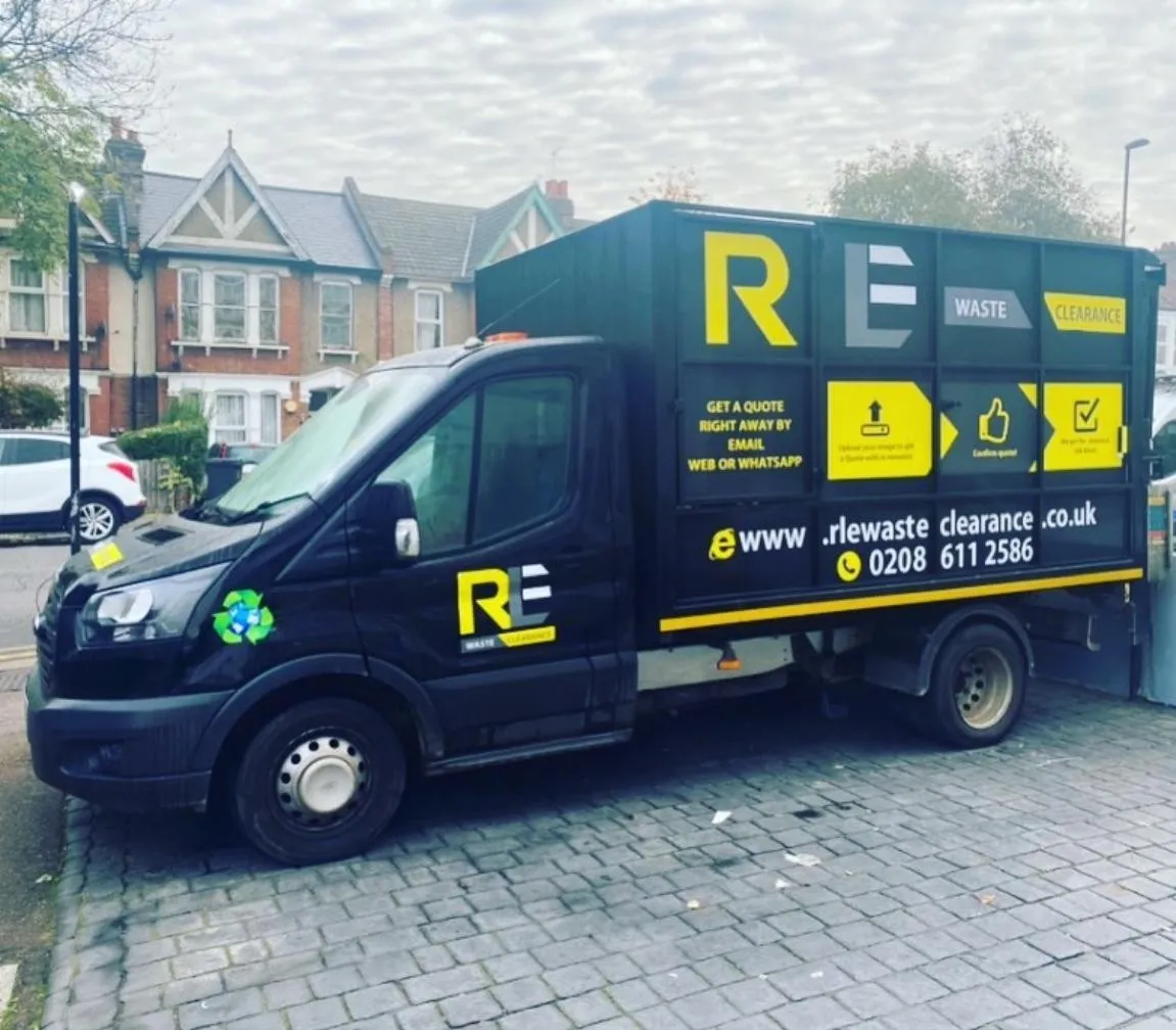 RLE Waste Clearance truck in black and yellow livery parked on block paving in front of a row of terraced houses