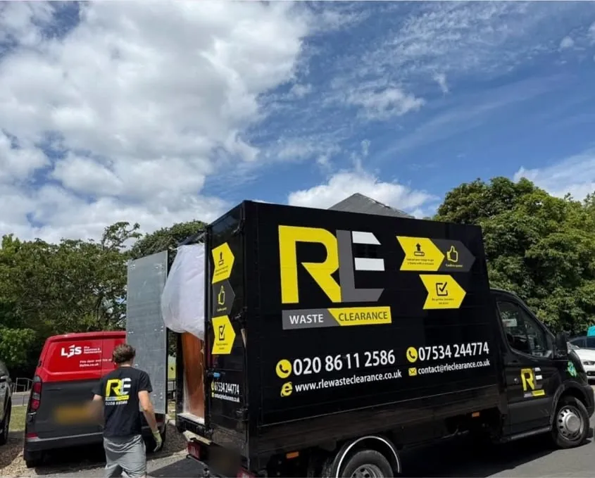 An RLE crew member walking to the open back of a black RLE Waste Clearance box truck under a blue sky