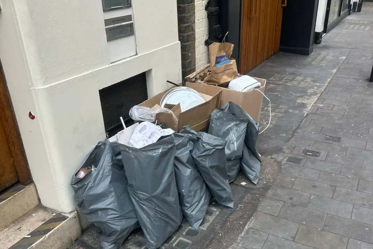 Before: Grey sacks and cardboard boxes of waste piled on the pavement beside a building entrance and its wooden doors