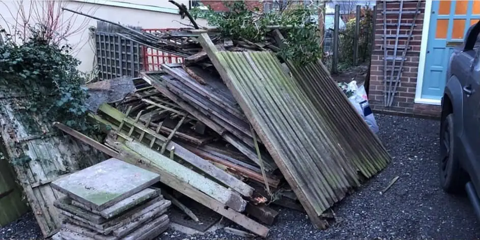 Before: Broken fence panels, timber and paving slabs piled in a front garden beside a house with a blue door