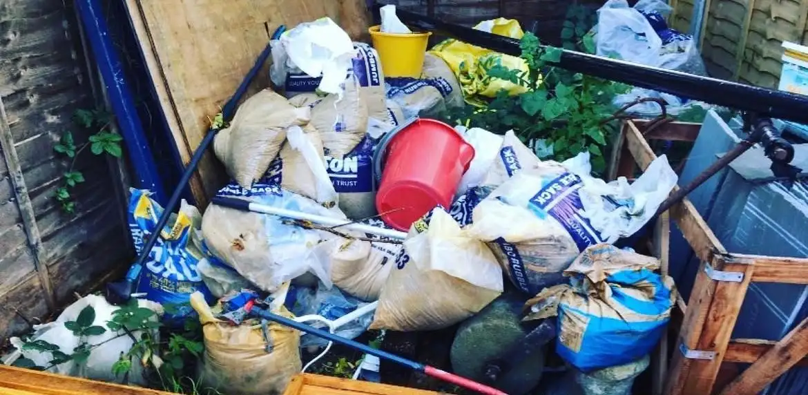 Before: Builders' sacks of soil and rubble, buckets, pipes and timber against a garden fence beside a crate of paving slabs