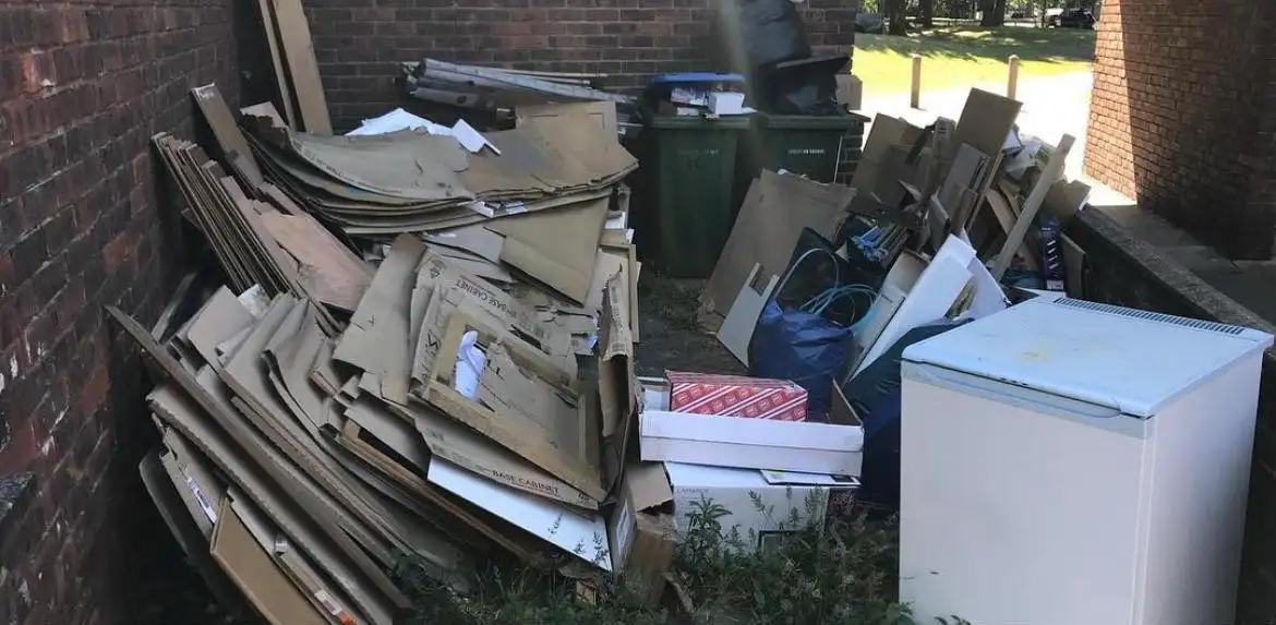 Before: Flattened cardboard, boxes, bags and a small white fridge piled in a brick bin store beside green wheelie bins