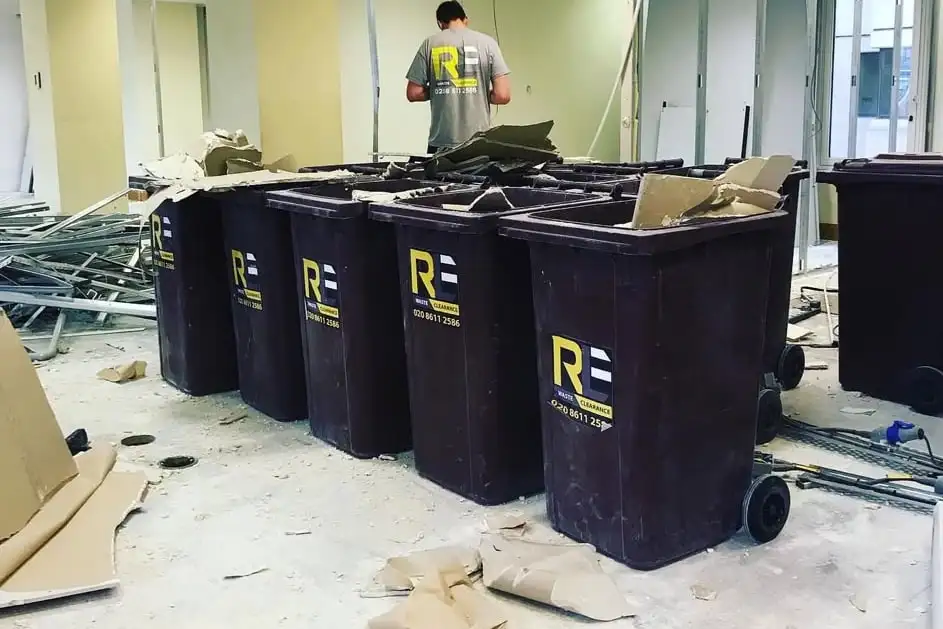 RLE-branded wheelie bins filled with metal studs and board from an office strip-out, with a crew member working behind them