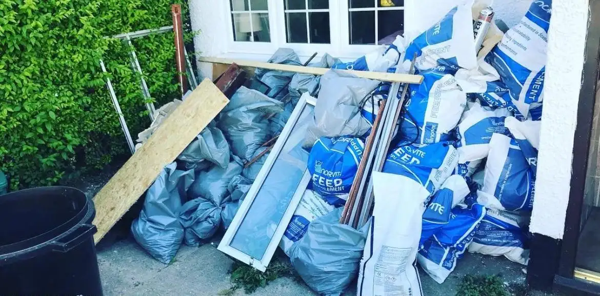 Before: Rubble and feed sacks, a uPVC window frame, timber and a chipboard sheet piled under a front window beside a hedge