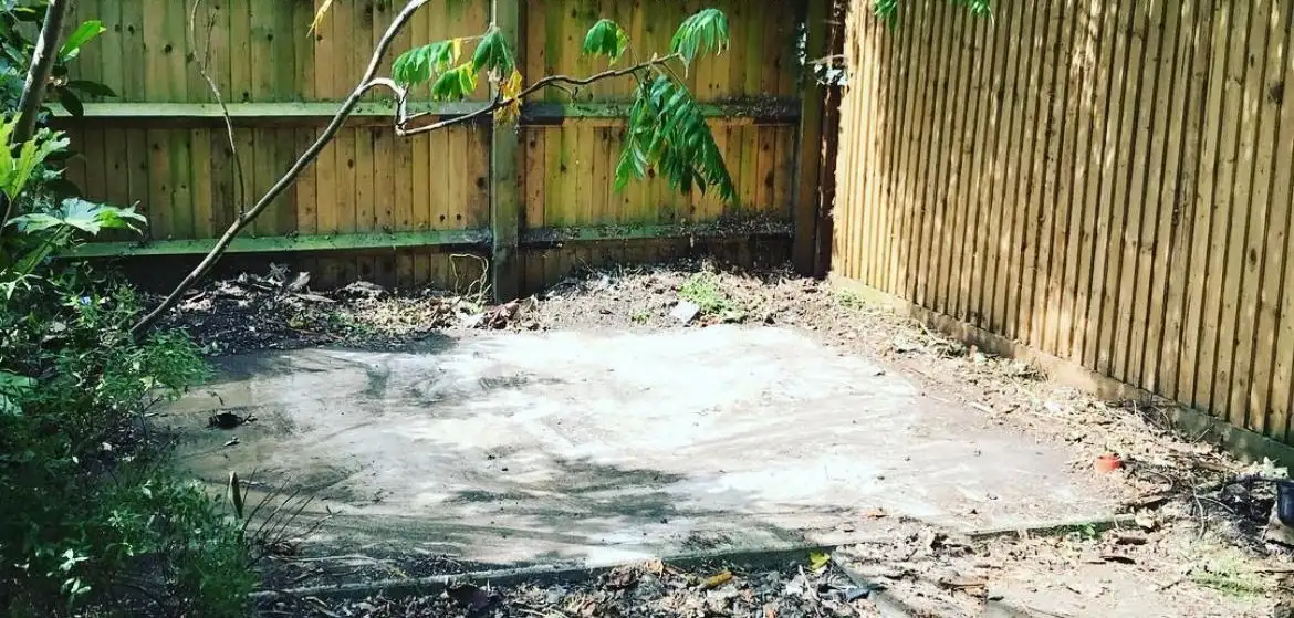 After: The shed removed, leaving a bare concrete base between garden fences