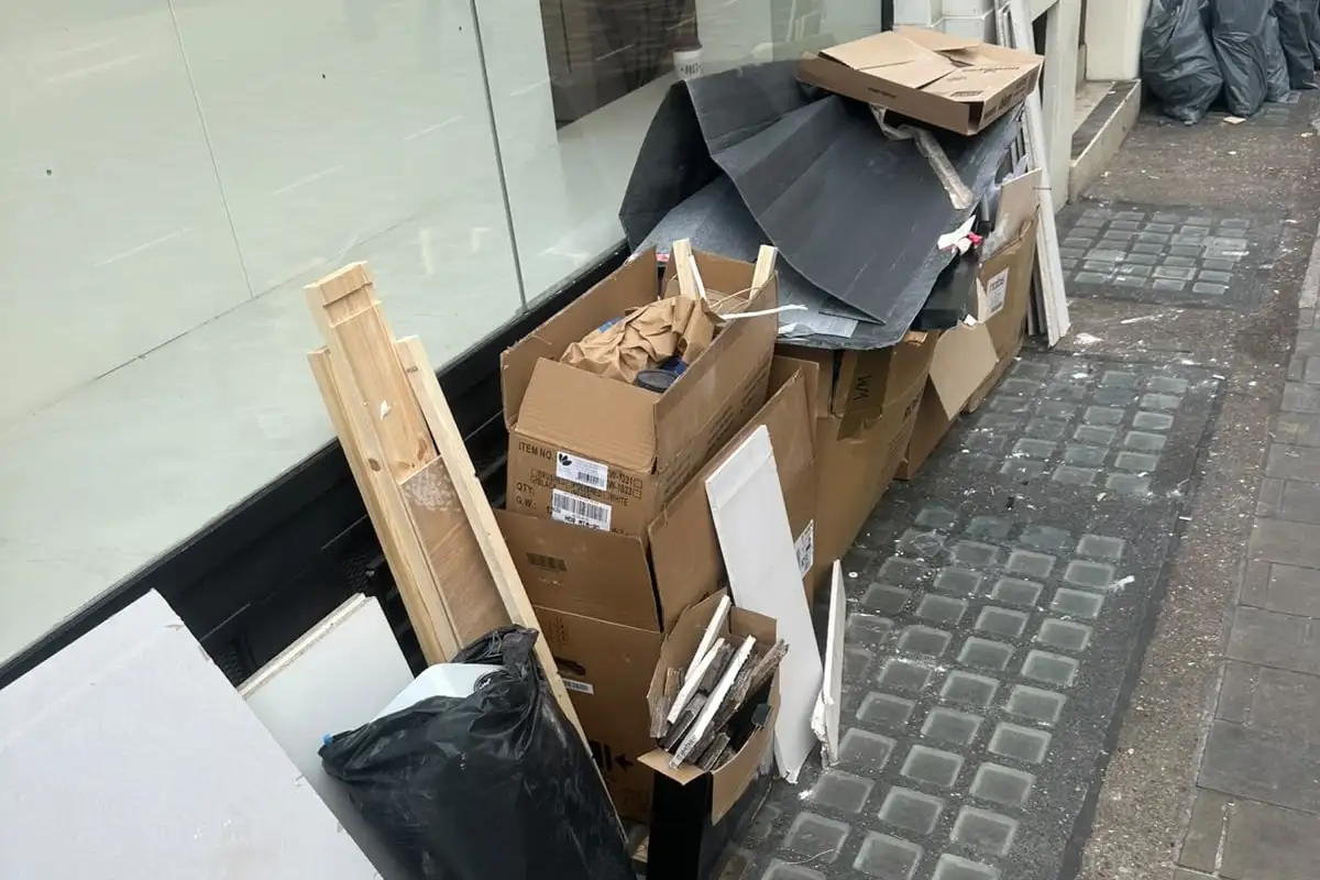 Before: Cardboard boxes, timber battens, white boards and black sheeting stacked against a shop window on the pavement