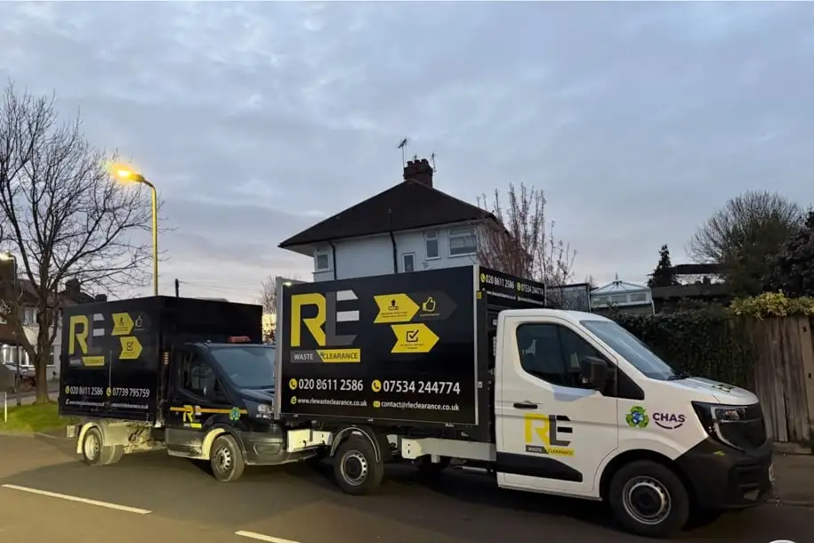 Two RLE Waste Clearance trucks, a black box truck and a white tipper, parked on a residential street at dusk