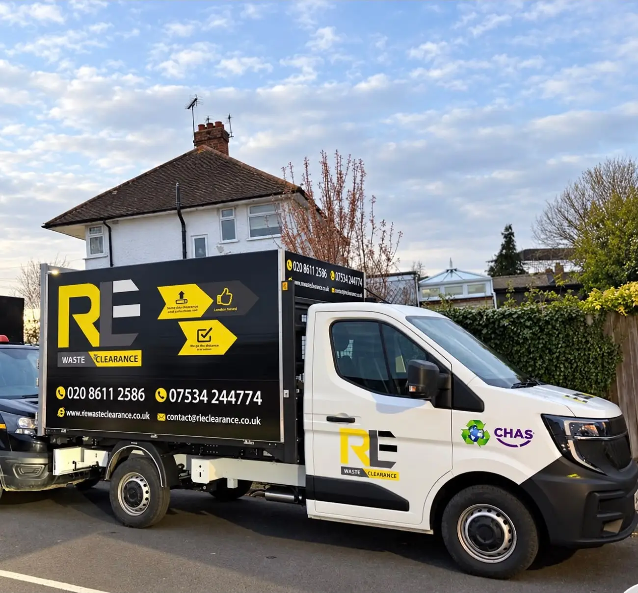 RLE Waste Clearance truck with a white cab and a black box body showing the RLE logo and phone numbers, parked on a residential street in front of a white semi-detached house